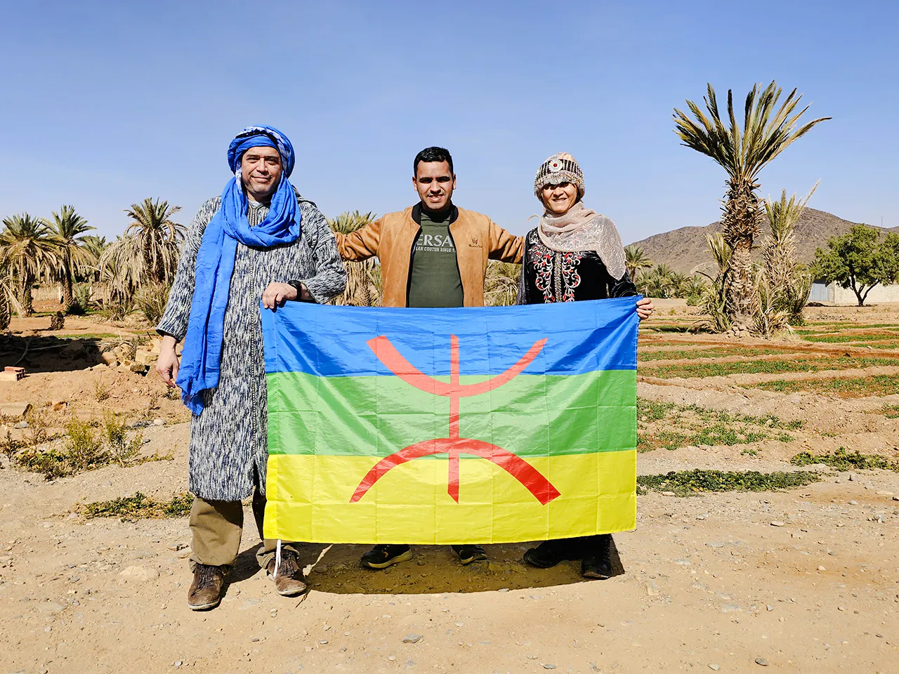 Three people holding a Berber flag in the Zagora Desert, Morocco.