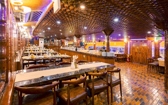 Interior dining area of Alexandra VIP Dhow Cruise with set tables and ornate wooden decor.
