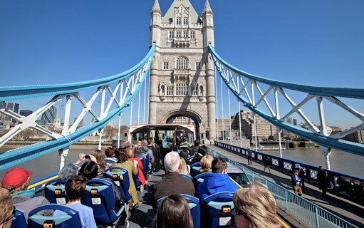 Tourists on Tootbus crossing Tower Bridge, London, with cityscape in the background.