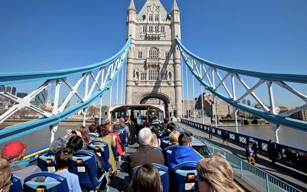 Tourists on Tootbus crossing Tower Bridge, London, with cityscape in the background.