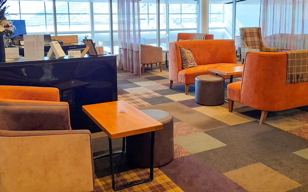 Plaza Premium Lounge seating area with orange sofas and tables near large windows.