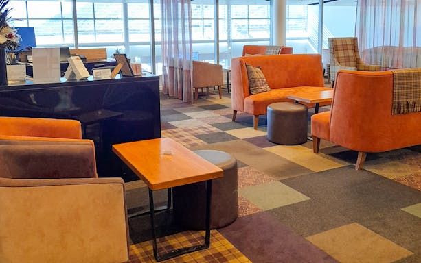 Plaza Premium Lounge seating area with orange sofas and tables near large windows.