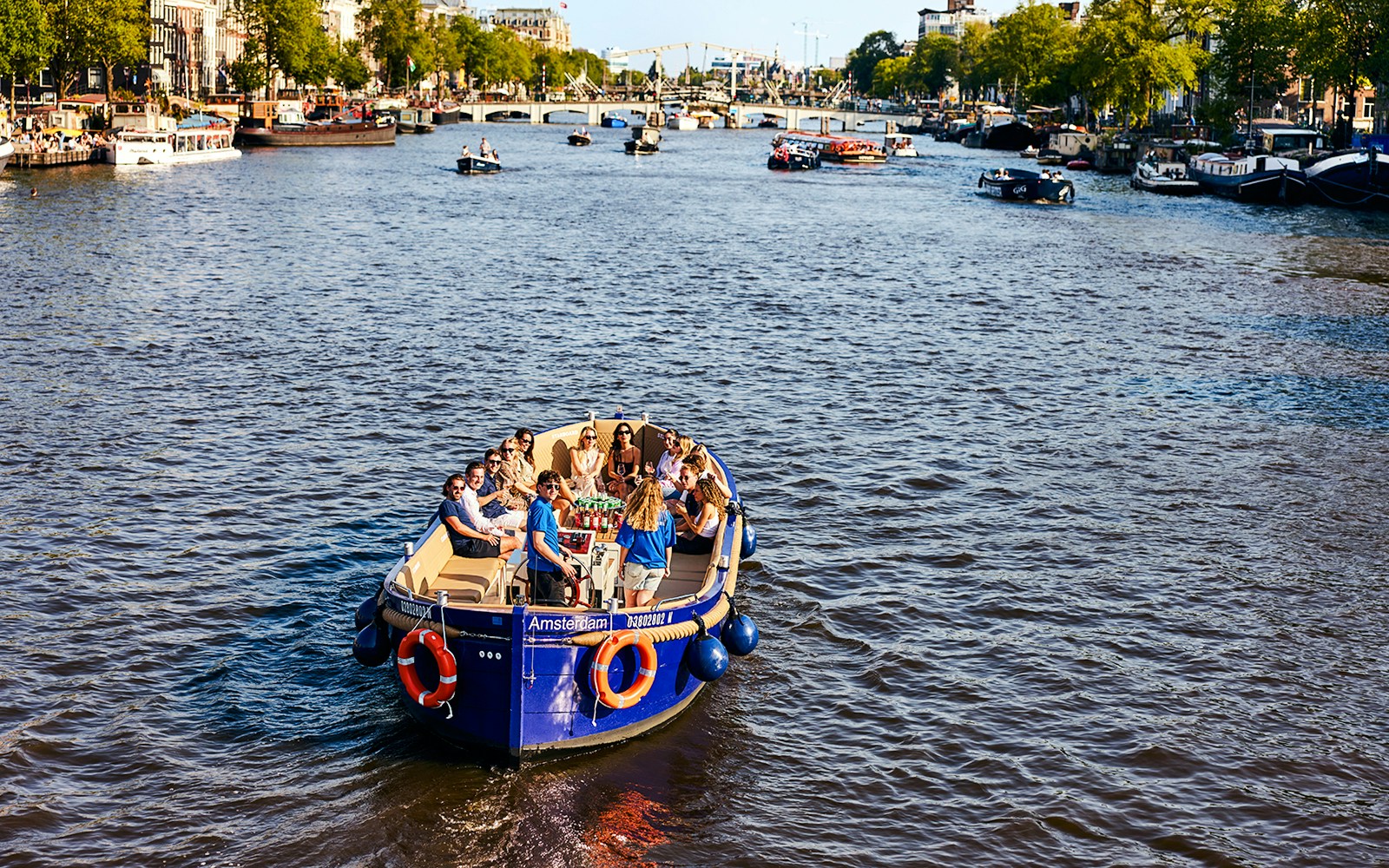 Amsterdam canal boat cruising under historic bridge.