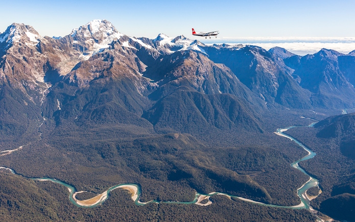 Aerial view of Milford Sound mountains with a plane flying over, showcasing scenic flyover from Queenstown.