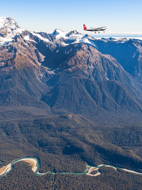Aerial view of Milford Sound mountains with a plane flying over, showcasing scenic flyover from Queenstown.