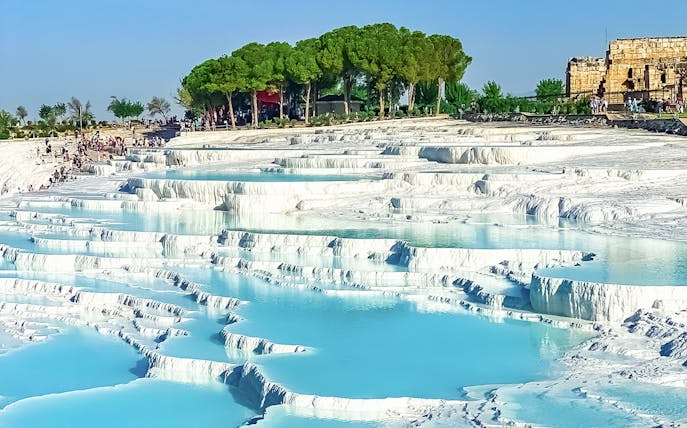Terraced thermal pools of Pamukkale with tourists exploring the site in Turkey.
