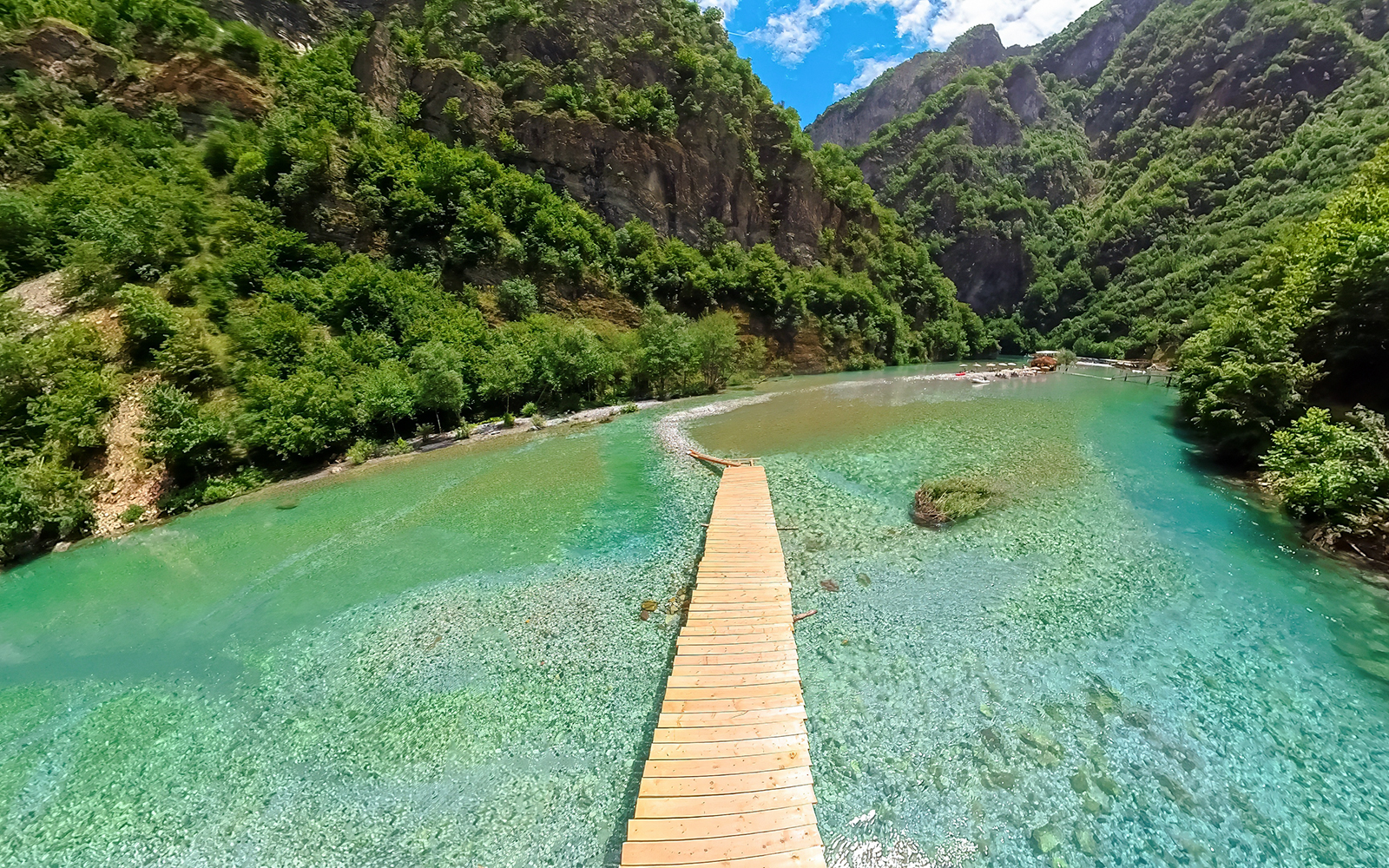 Wooden walkway over Shala River with lush green mountains during Komani Lake tour from Tirana.