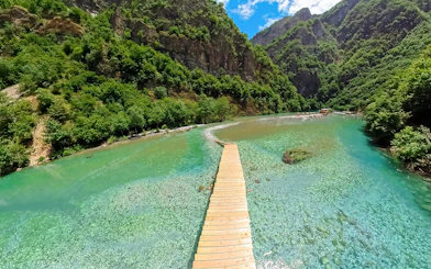 Wooden walkway over Shala River with lush green mountains during Komani Lake tour from Tirana.