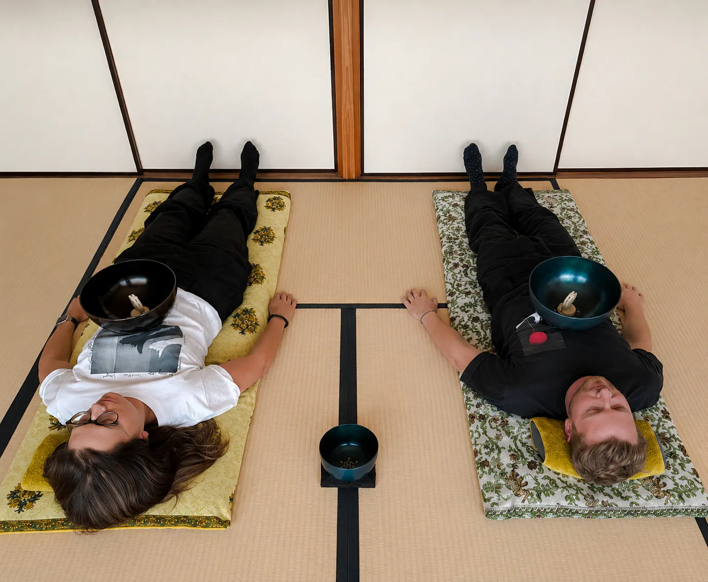 Two people lying on mats with sound bowls on their chests during a Japanese sound bath in Kyoto.