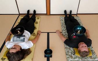 Two people lying on mats with sound bowls on their chests during a Japanese sound bath in Kyoto.