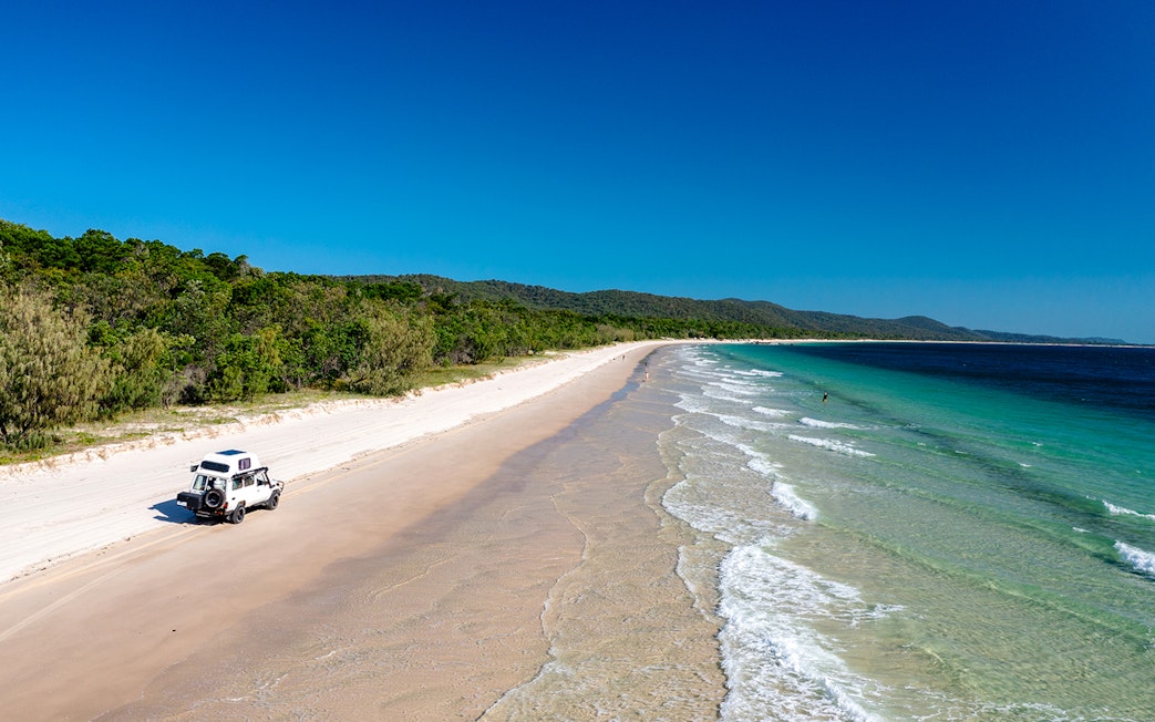 4WD vehicle driving along Moreton Island beach, highlighting offroad adventure.
