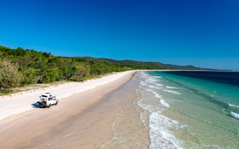 4WD vehicle driving along Moreton Island beach, highlighting offroad adventure.