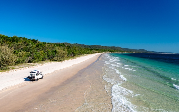 4WD vehicle driving along Moreton Island beach, highlighting offroad adventure.