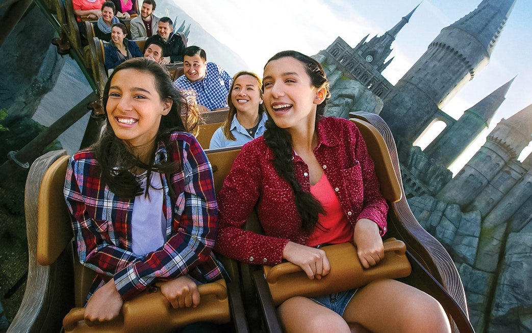 Visitors enjoying a roller coaster at Universal Studios Hollywood with Hogwarts Castle in the background.