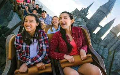 Visitors enjoying a roller coaster at Universal Studios Hollywood with Hogwarts Castle in the background.