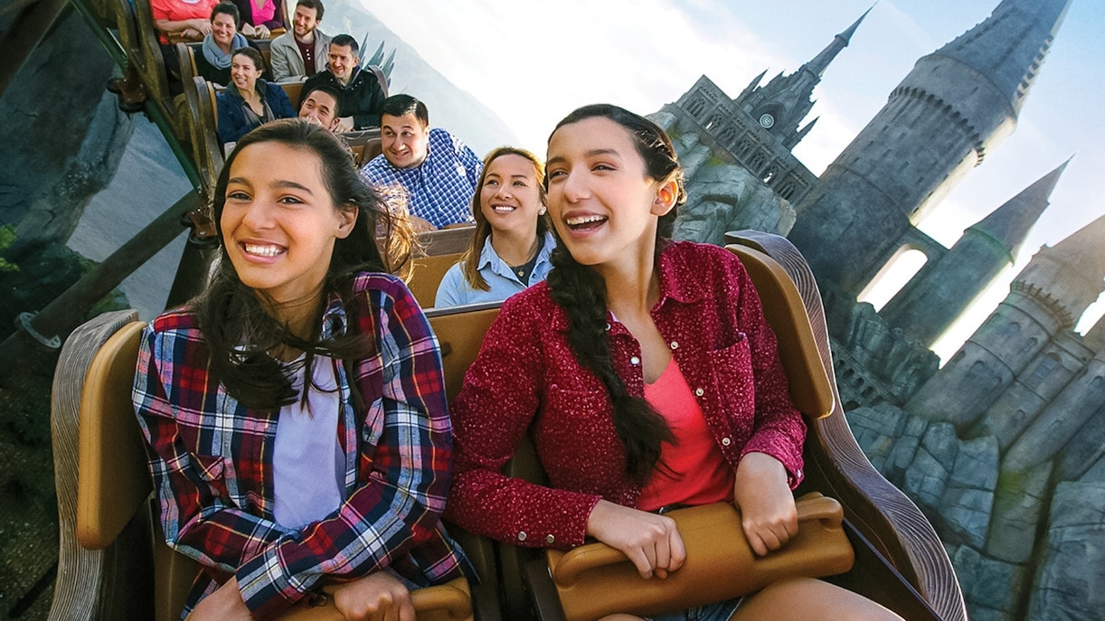 Visitors enjoying a roller coaster at Universal Studios Hollywood with Hogwarts Castle in the background.