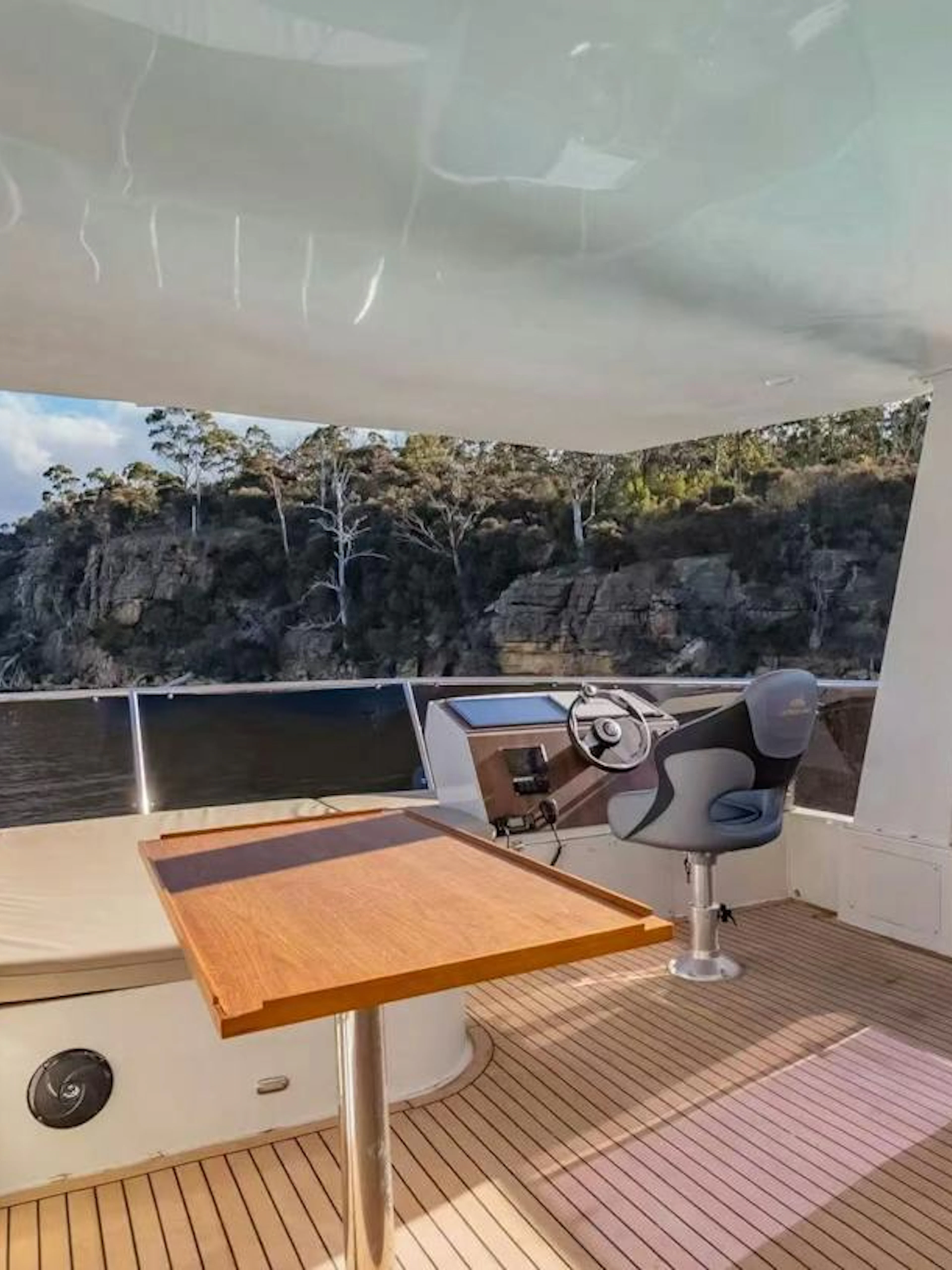 Private yacht deck with seating and steering area, scenic view of Hobart coastline.