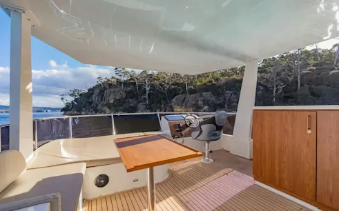Private yacht deck with seating and steering area, scenic view of Hobart coastline.