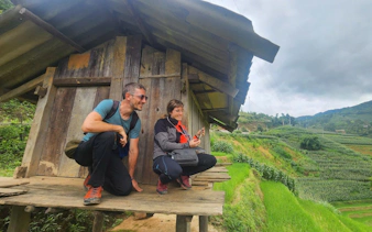 Tourists with a local guide at a wooden hut overlooking rice terraces in Mu Cang Chai, Vietnam.