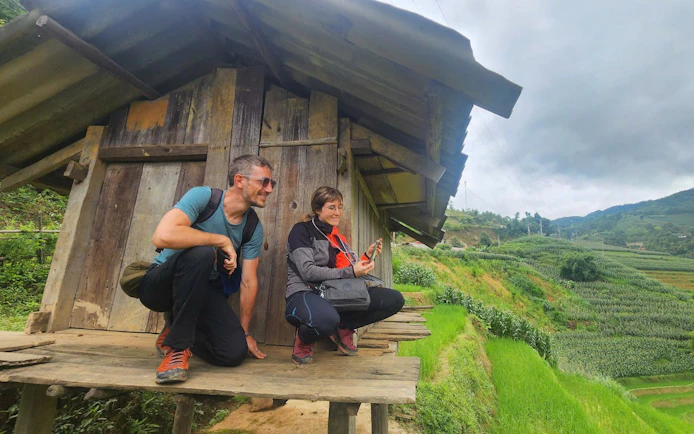 Tourists with a local guide at a wooden hut overlooking rice terraces in Mu Cang Chai, Vietnam.