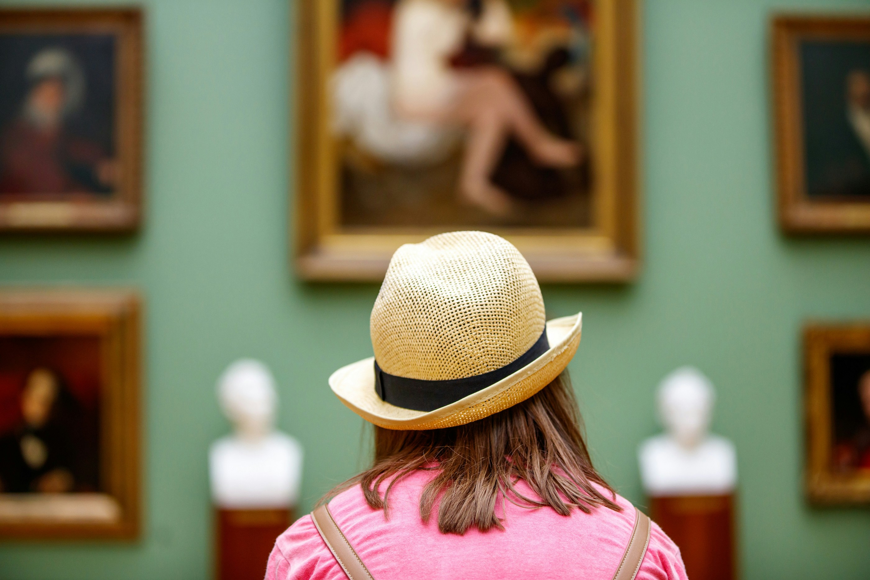 Girl in a hat viewing paintings in a museum gallery.