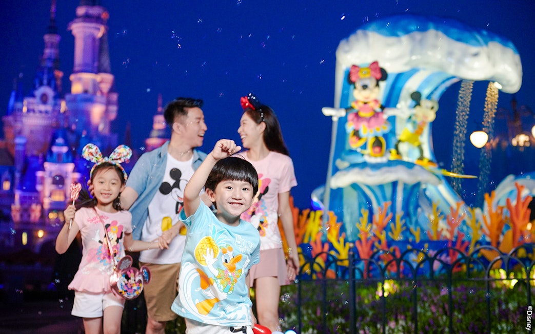 Family enjoying attractions at Shanghai Disneyland with castle and character statues in background.