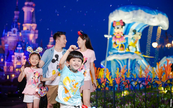 Family enjoying attractions at Shanghai Disneyland with castle and character statues in background.