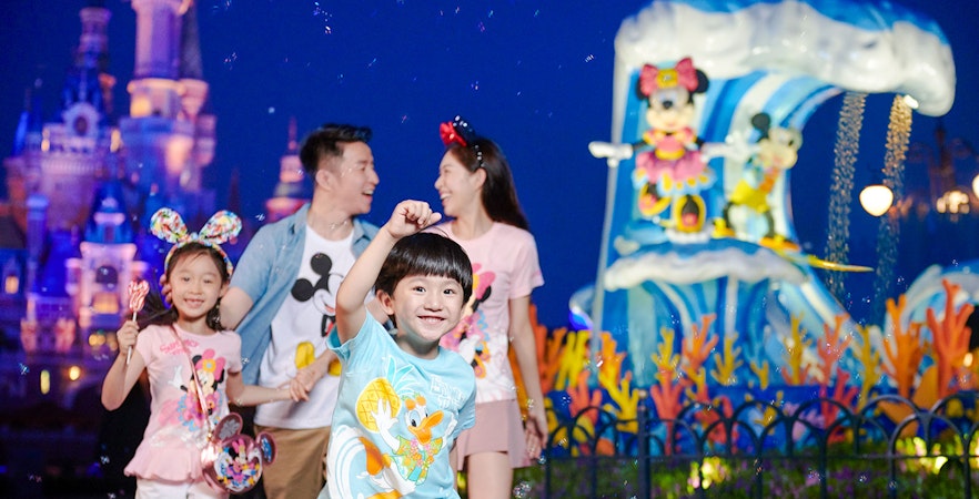 Family enjoying attractions at Shanghai Disneyland with castle and character statues in background.