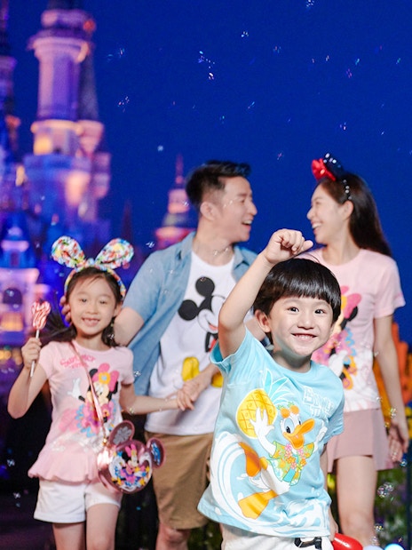 Family enjoying attractions at Shanghai Disneyland with castle and character statues in background.