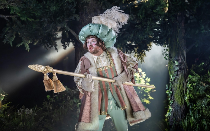 Performer in elaborate costume holding a staff on stage during "Into The Woods" production.