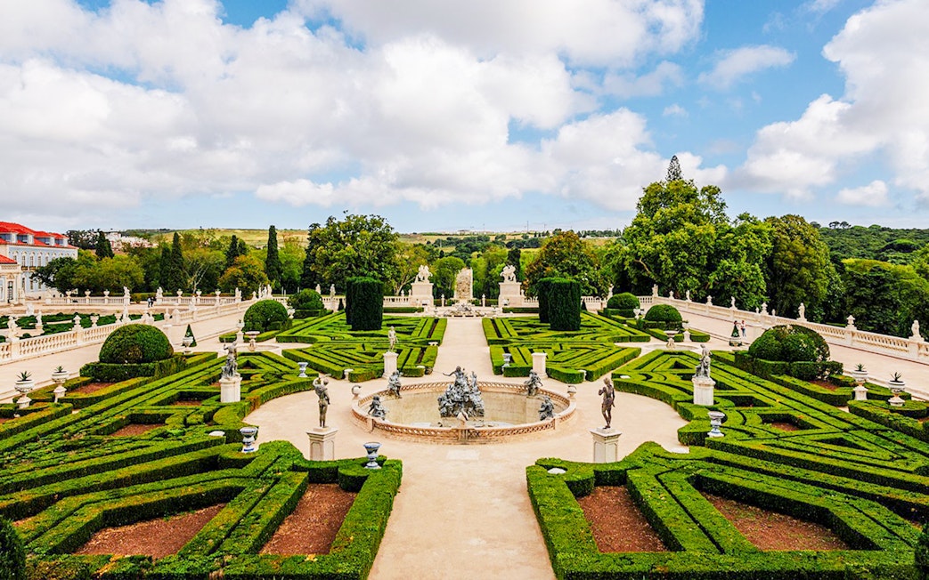 Upper garden of the National Palace of Queluz with manicured hedges and statues.