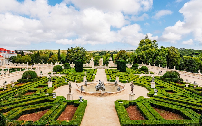 Upper garden of the National Palace of Queluz with manicured hedges and statues.