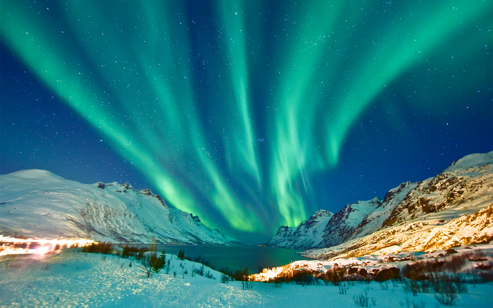 Northern lights over Tromso, Norway, with snow-covered mountains and a starry sky.