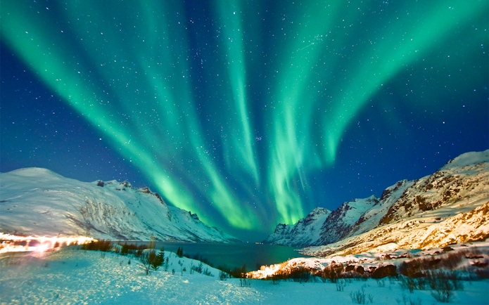 Northern lights over Tromso, Norway, with snow-covered mountains and a starry sky.