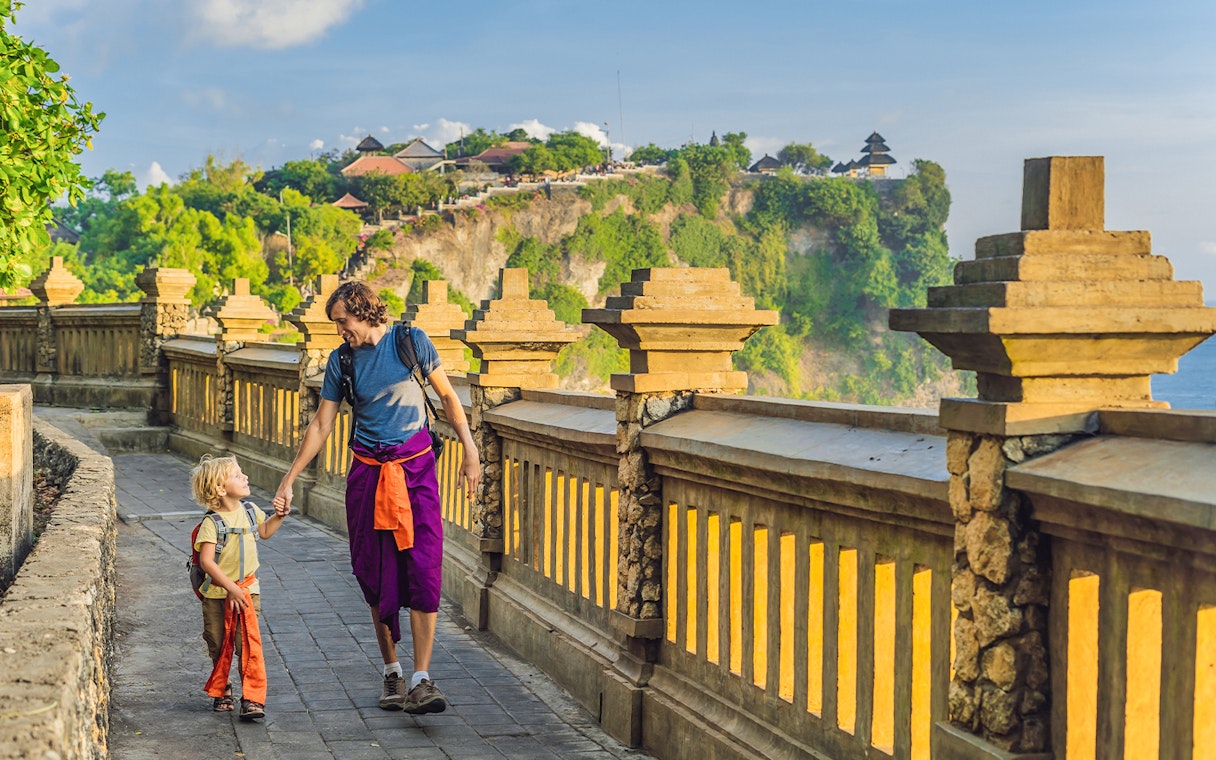 Visitors walking along the path at Uluwatu Temple, Bali, with ocean view.