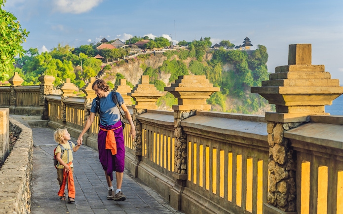 Visitors walking along the path at Uluwatu Temple, Bali, with ocean view.