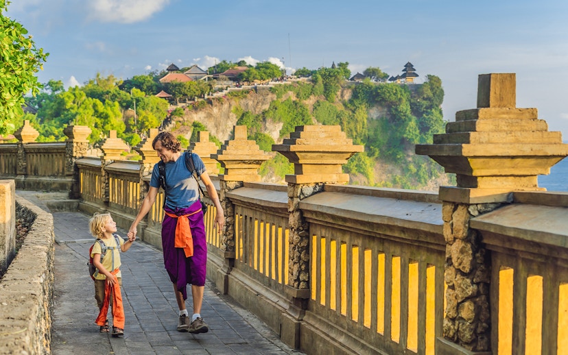 Visitors walking along the path at Uluwatu Temple, Bali, with ocean view.