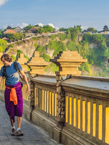 Visitors walking along the path at Uluwatu Temple, Bali, with ocean view.