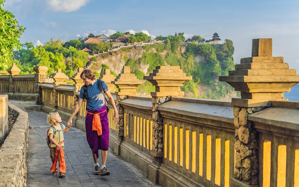 Visitors walking along the path at Uluwatu Temple, Bali, with ocean view.