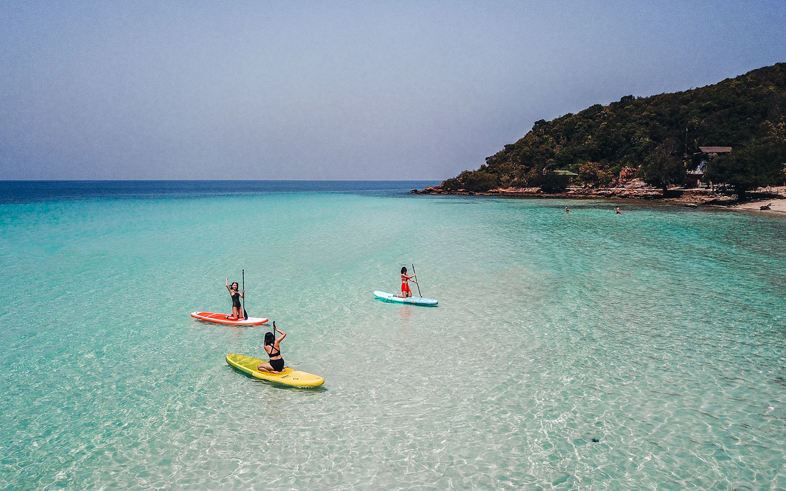 Paddleboarders on clear waters near Pattaya Island, Thailand, with lush coastline.