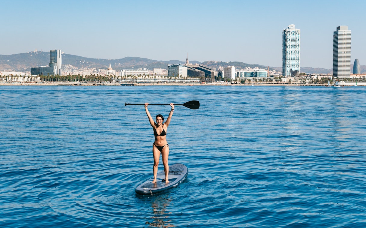 Tourist paddleboarding near Barcelona skyline on a sightseeing cruise.