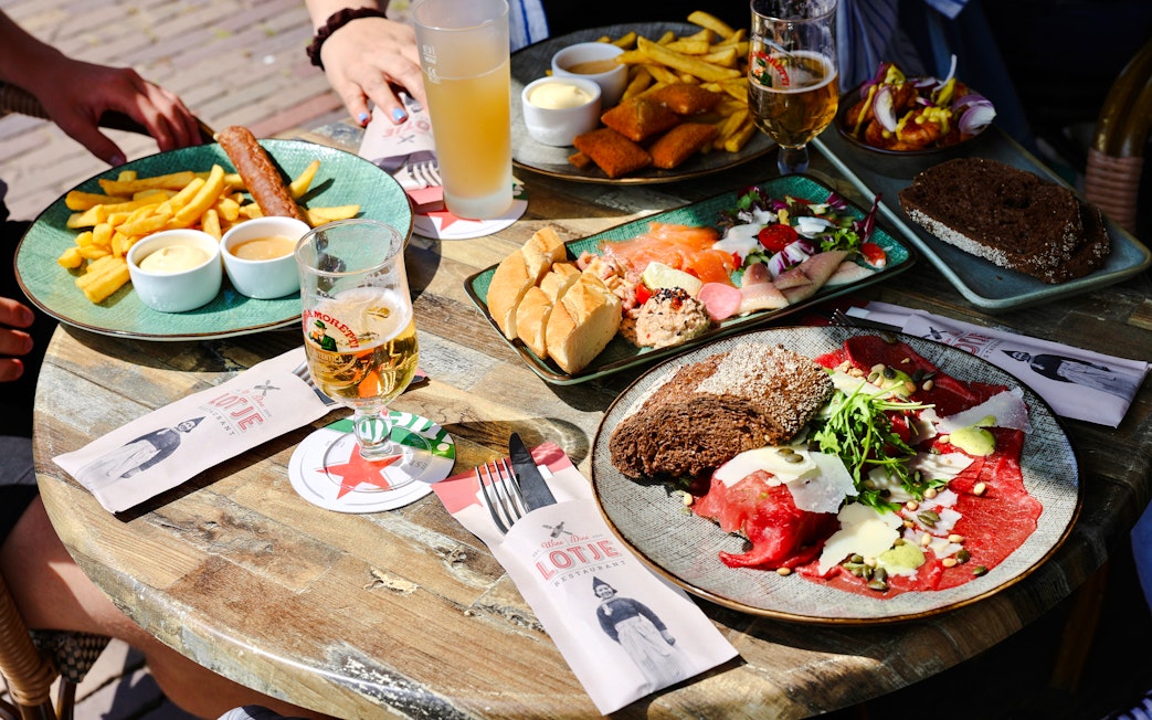 Local cuisine and beverages on a table in Volendam, featuring assorted meats, bread, and drinks.
