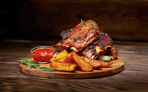 Barbecue ribs and potato wedges served on a wooden platter for Danube sunset cruise.