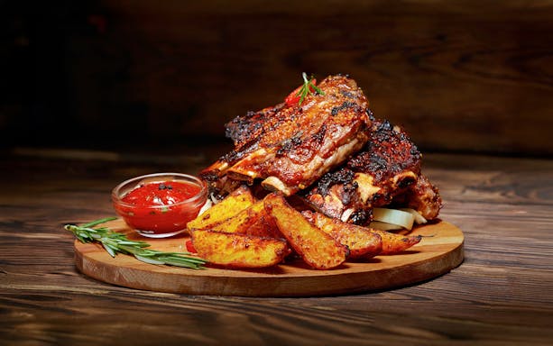 Barbecue ribs and potato wedges served on a wooden platter for Danube sunset cruise.