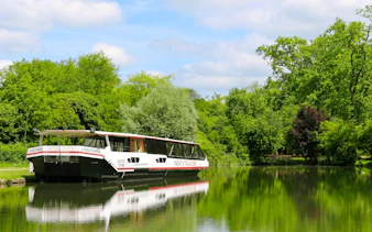 Tour boat on Canal du Midi in Toulouse surrounded by lush greenery.
