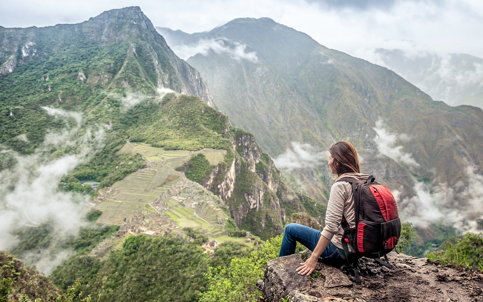 Girl hiker atop Huayna Picchu overlooking Machu Picchu ruins, Peru.