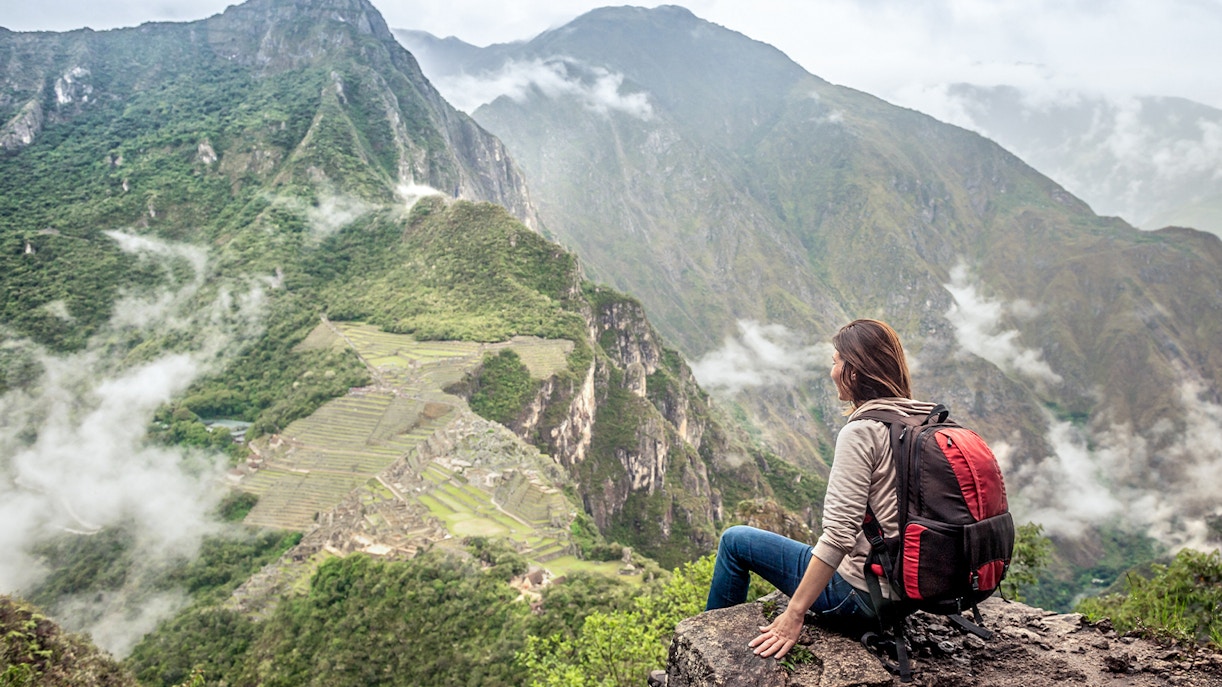 Hiker sitting on Huayna Picchu overlooking Machu Picchu, Peru.
