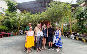 Group of tourists at a historic site in Ho Chi Minh City, surrounded by greenery and traditional architecture.