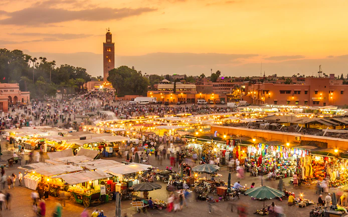 Jamaa el Fna market square bustling with people and stalls at sunset, Marrakesh, Morocco.