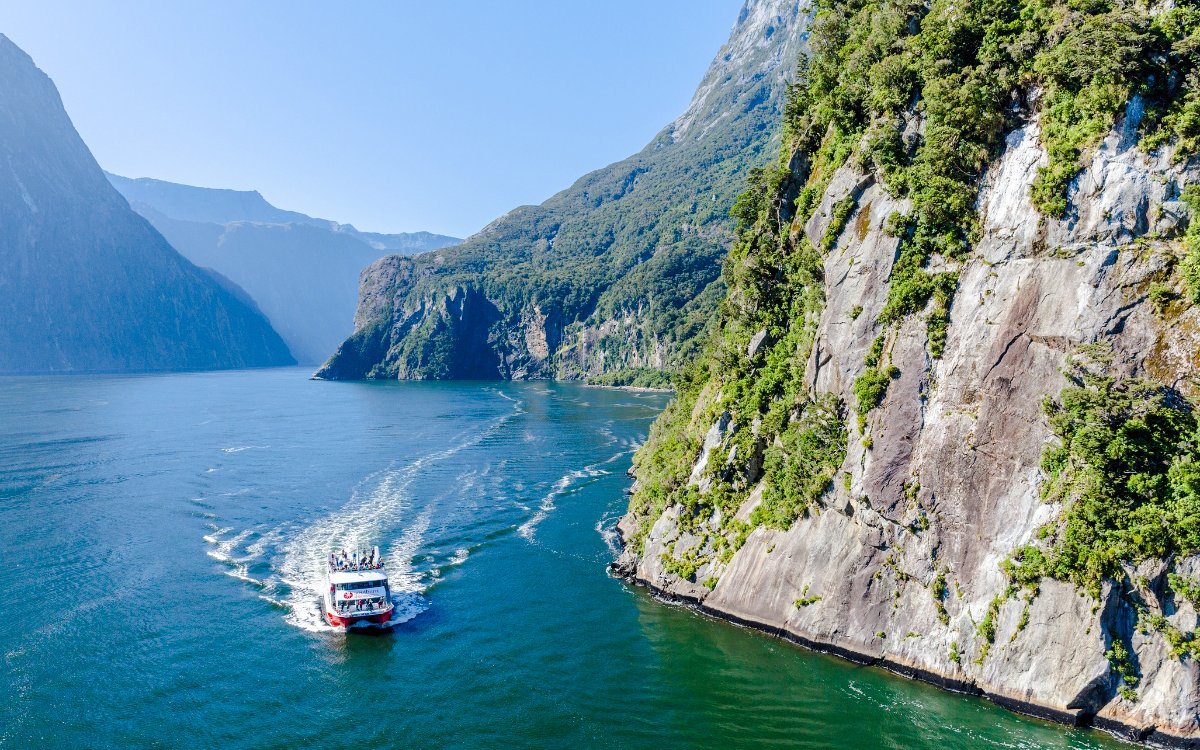 Cruise boat navigating Milford Sound with lush cliffs and clear water.